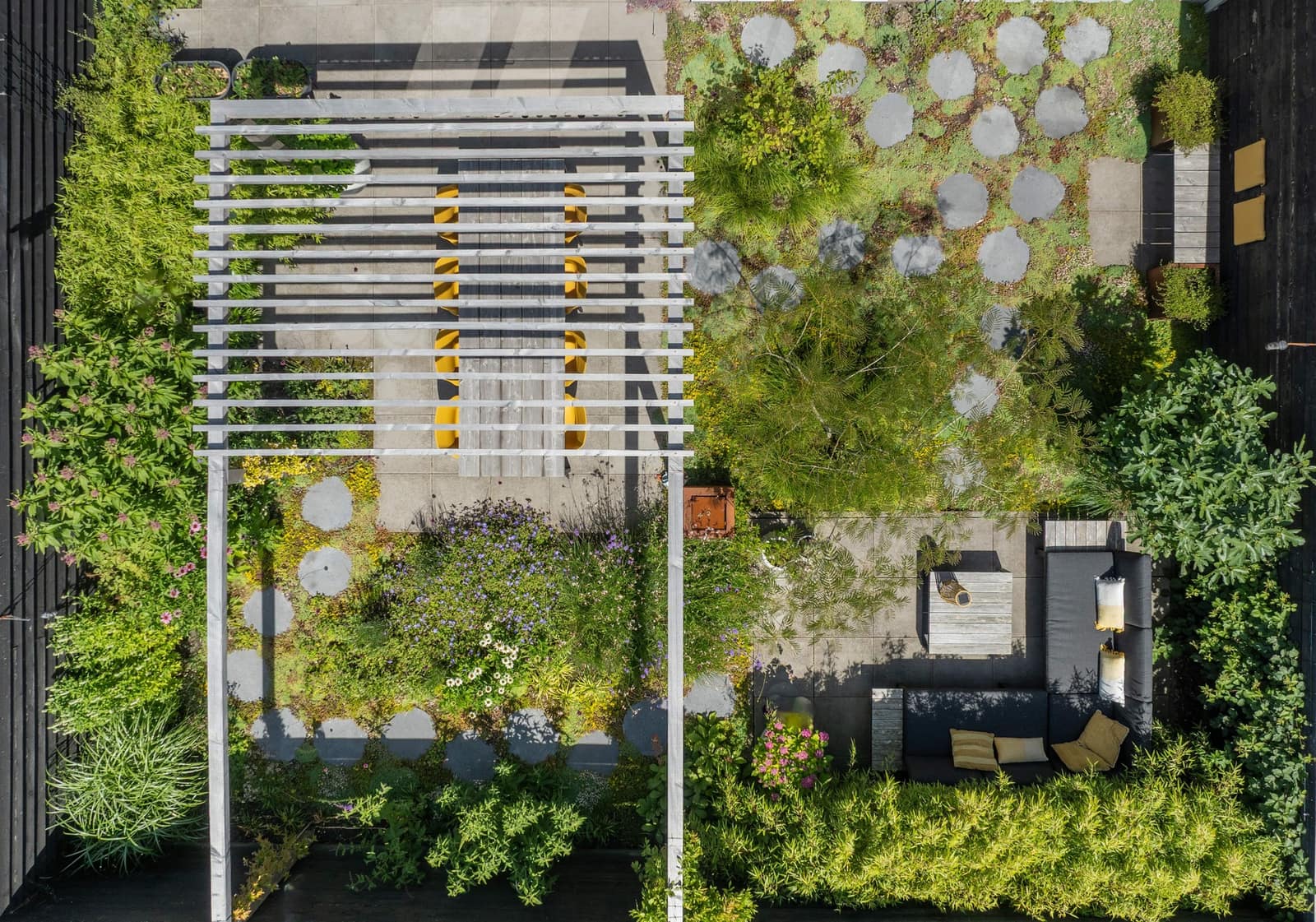 Relaxtuin van bovenaf: pergola met gele stoelen, ronde stapstenen en een loungehoek, aangelegd door Kars & Stoop